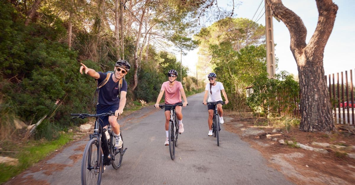 Cyclist leading the way with two friends following on a serene road, bordered by lush greenery.