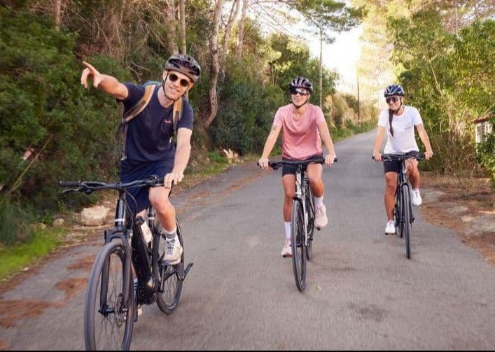 Cyclist leading the way with two friends following on a serene road, bordered by lush greenery.