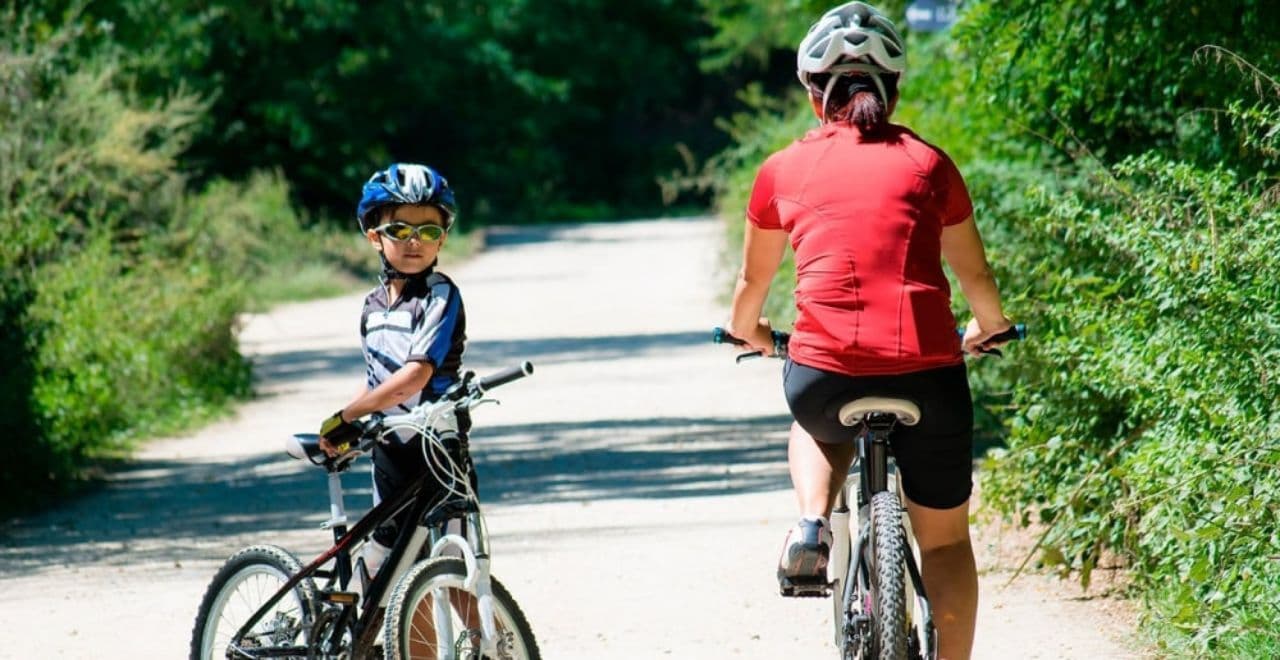 Mother and son biking on shaded dirt path through trees
