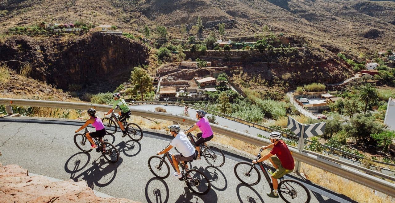 Cyclists navigating a winding mountain road with a village below.