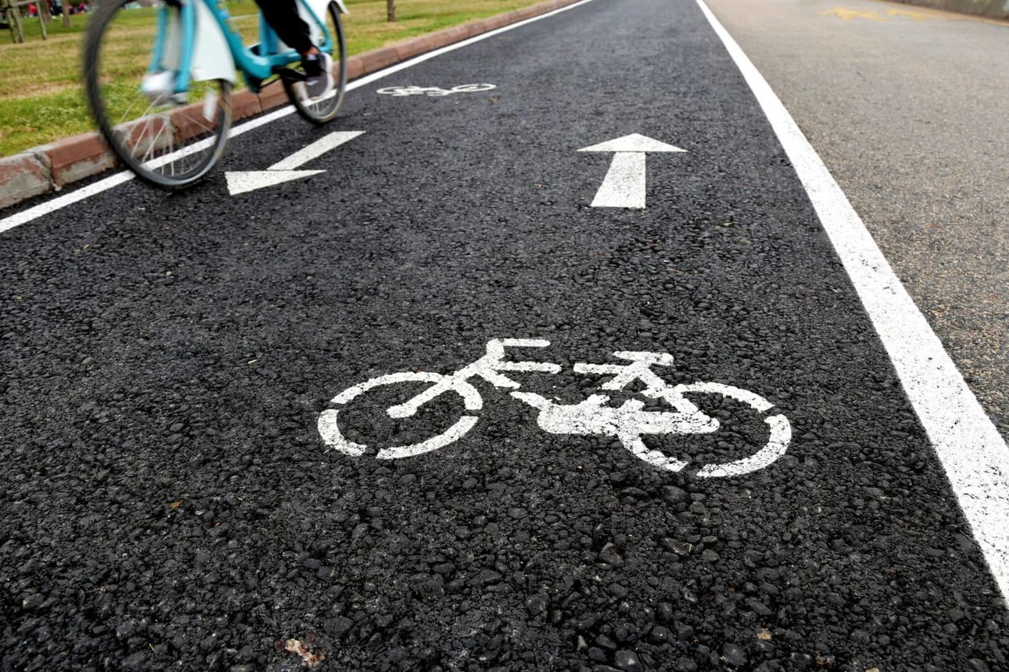 A cyclist riding on a dedicated bike lane with white bicycle symbols and directional arrows painted on the asphalt, emphasizing the importance of following the Highway Code for safe cycling.