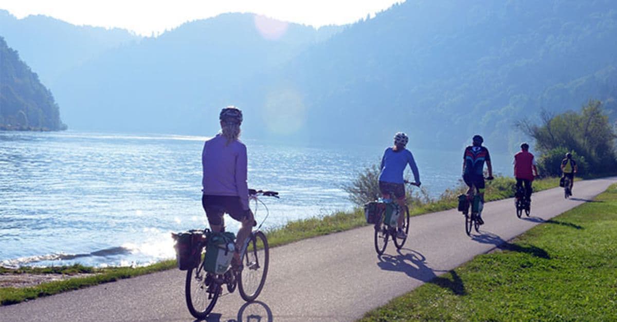 Group of cyclists enjoying a leisure ride along a riverside path with lush green mountains in the background