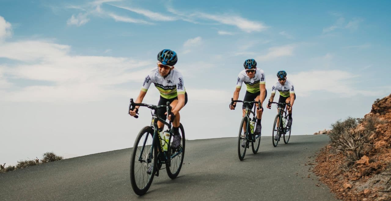 Cyclists riding on a winding road under a blue sky.