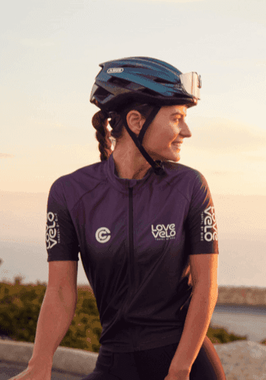 Cyclists in matching Love Velo apparel taking a break to enjoy a drink with a sunset over a calm sea in the background
