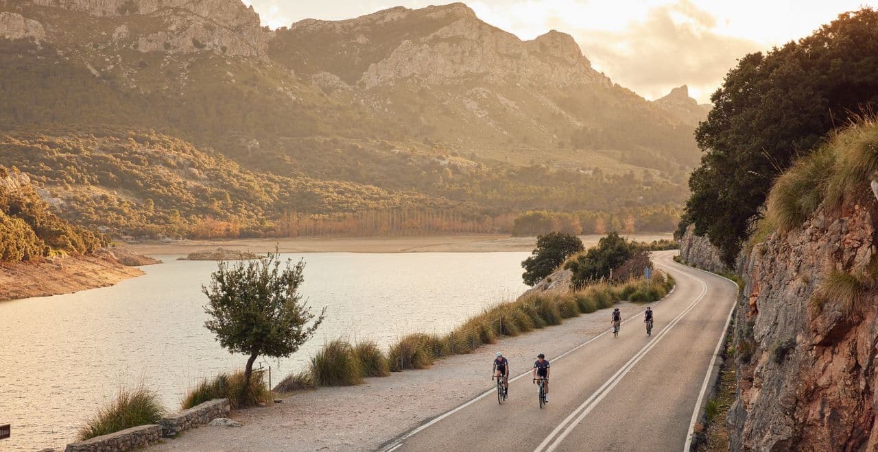 Cyclists riding along a lake with mountains in the background