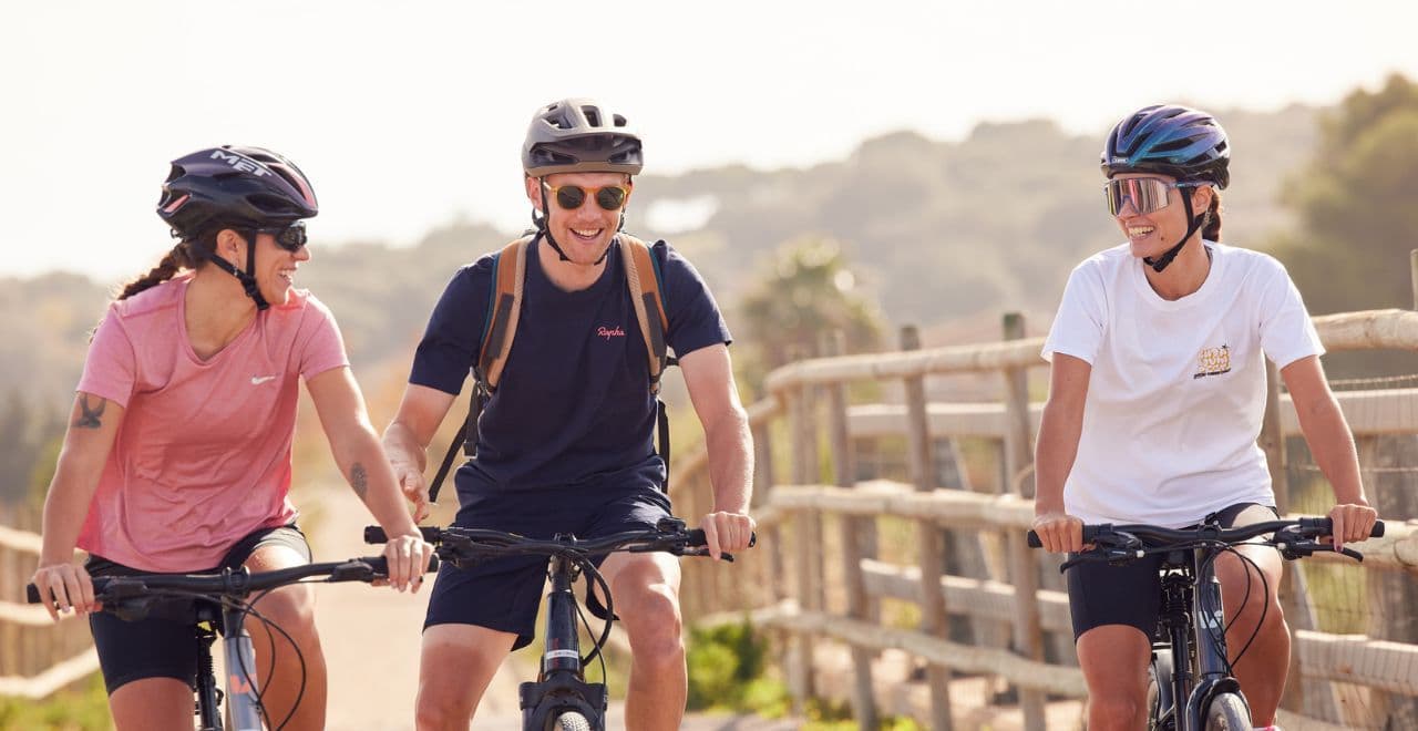 Three friends cycling on a sunny day, wearing helmets and sportswear.