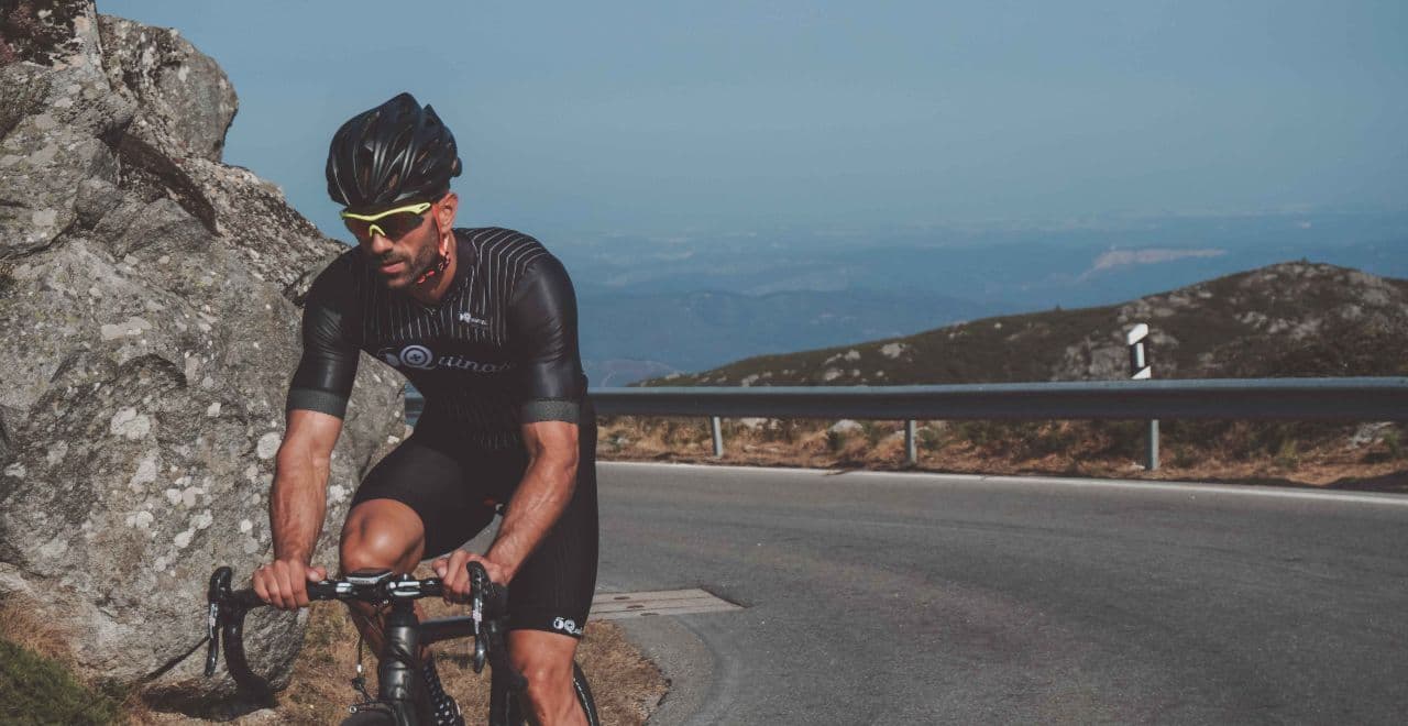 Close-up of a cyclist climbing a challenging mountain road, surrounded by rugged rocks and expansive mountain views.