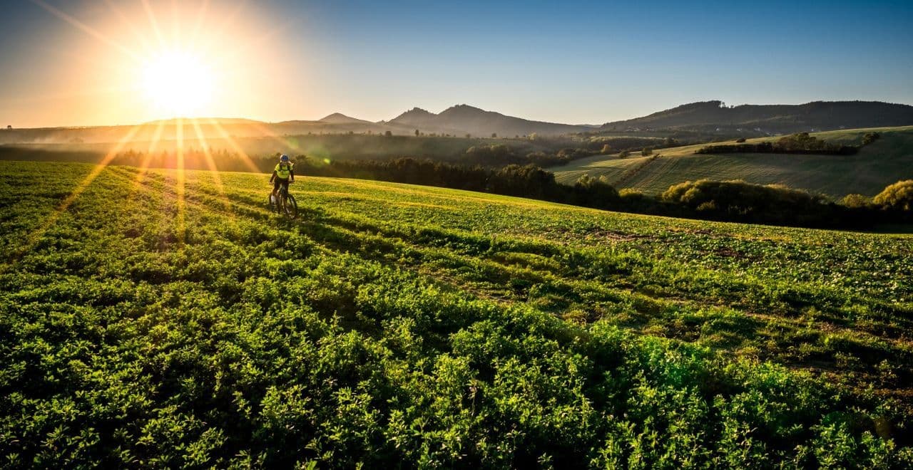 Cyclist riding through a field at sunset with lush green hills in the background