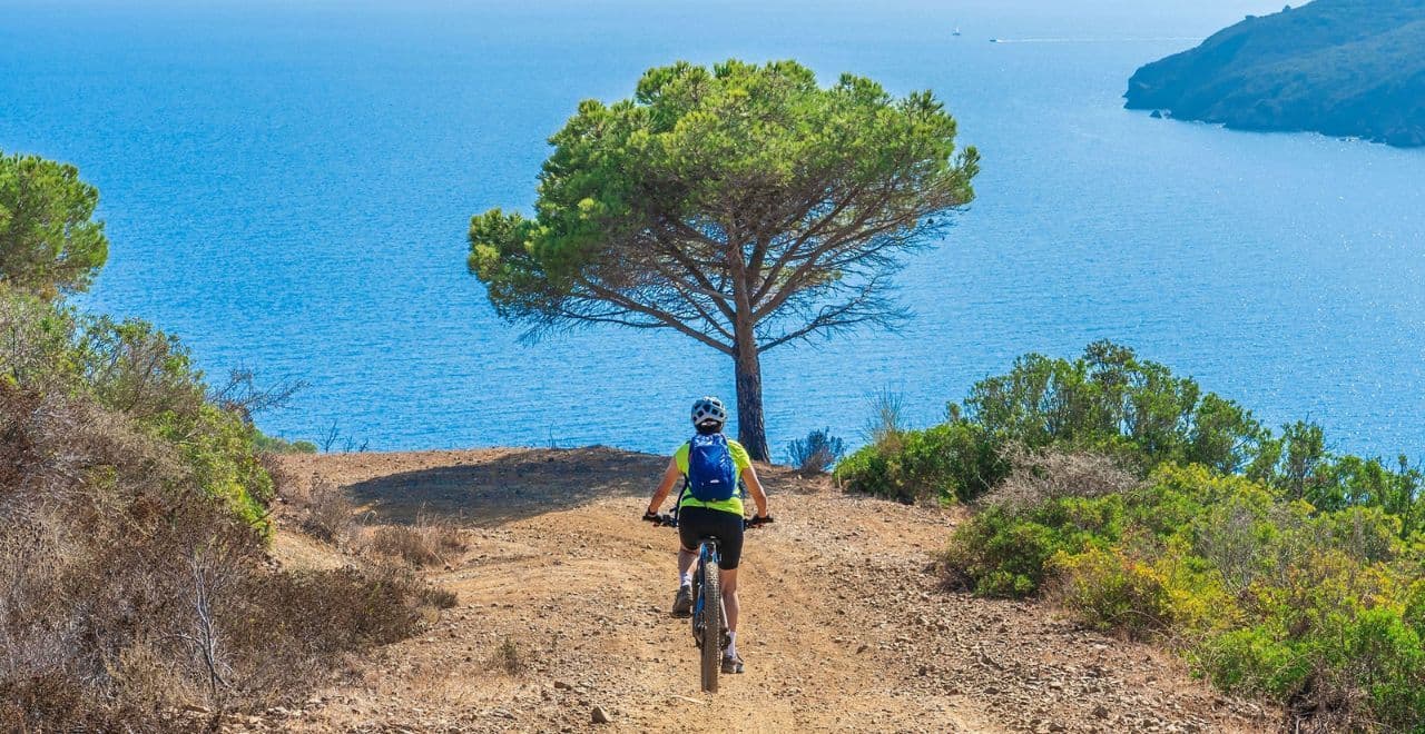 Mountain biker riding coastal trail toward bright blue sea