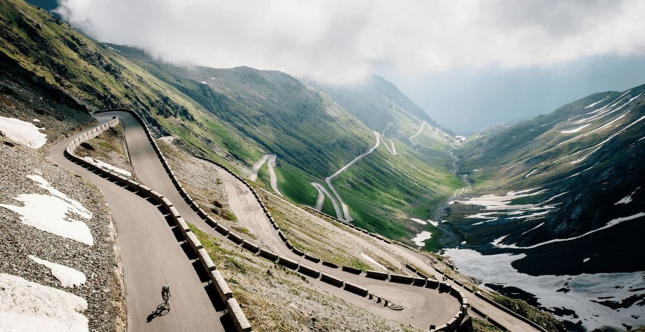 Cyclist climbing winding mountain pass with dramatic alpine switchbacks