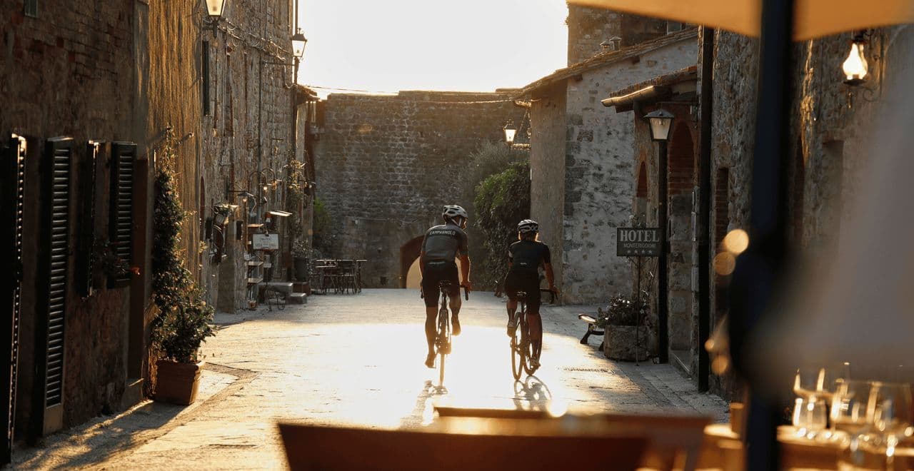 Two cyclists riding through narrow cobbled street at golden hour