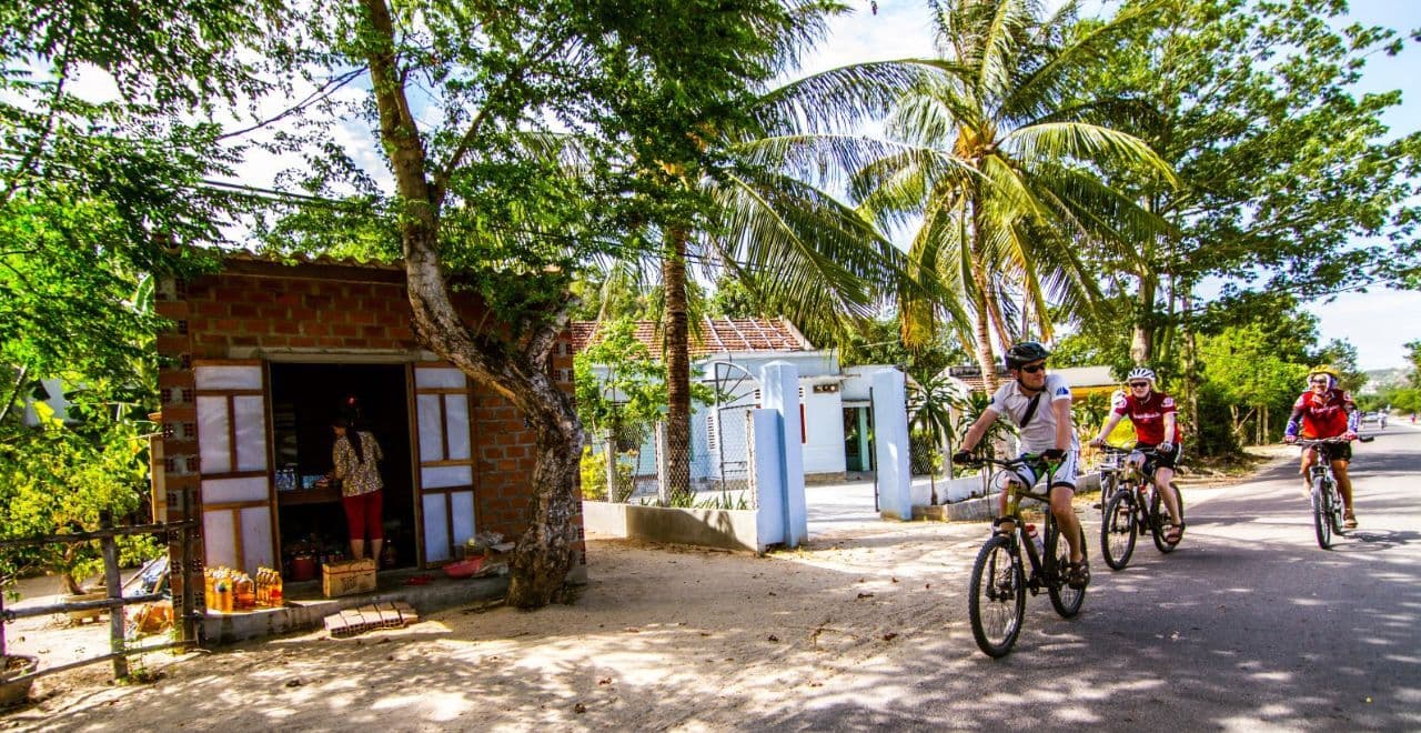 Cyclists exploring a quiet village in Vietnam, experiencing local life and tropical scenery on their cycling tour