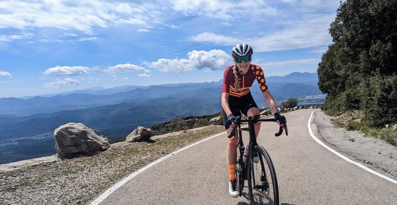 female cyclist riding up a mountain road with the valley and mountains in the background