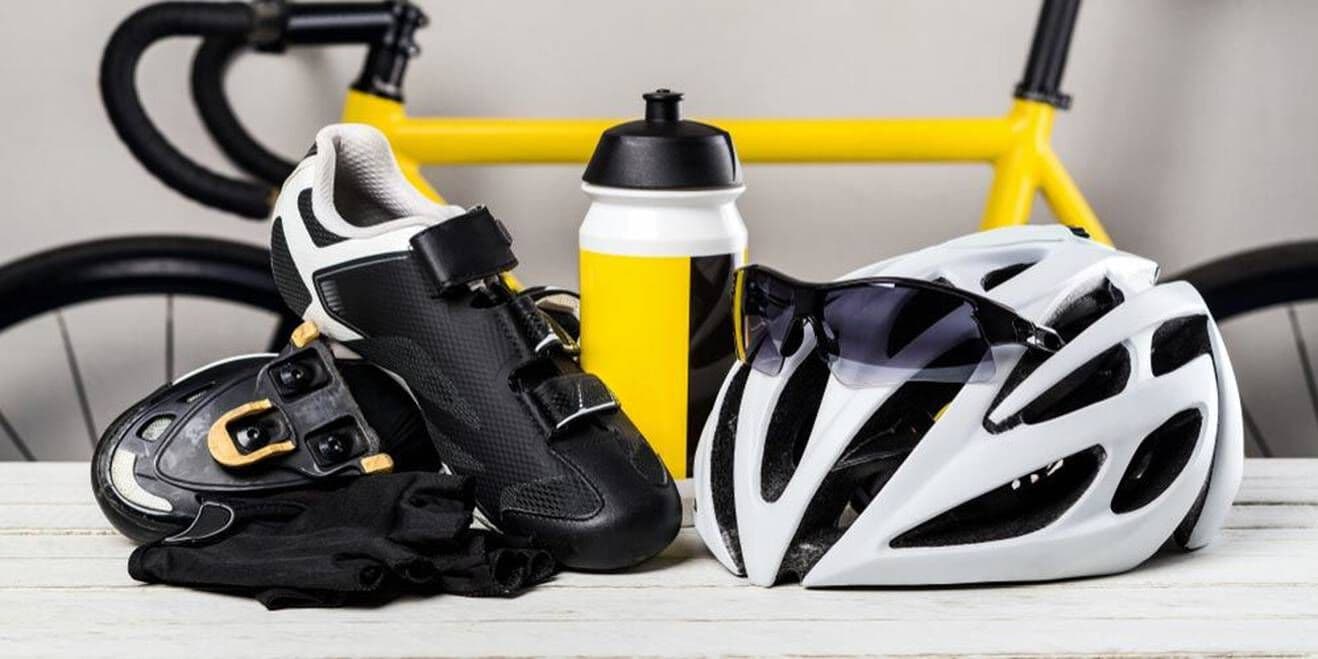 Essential cycling gear including cycling shoes, helmet, sunglasses, gloves, and a water bottle, with a yellow bicycle in the background.
