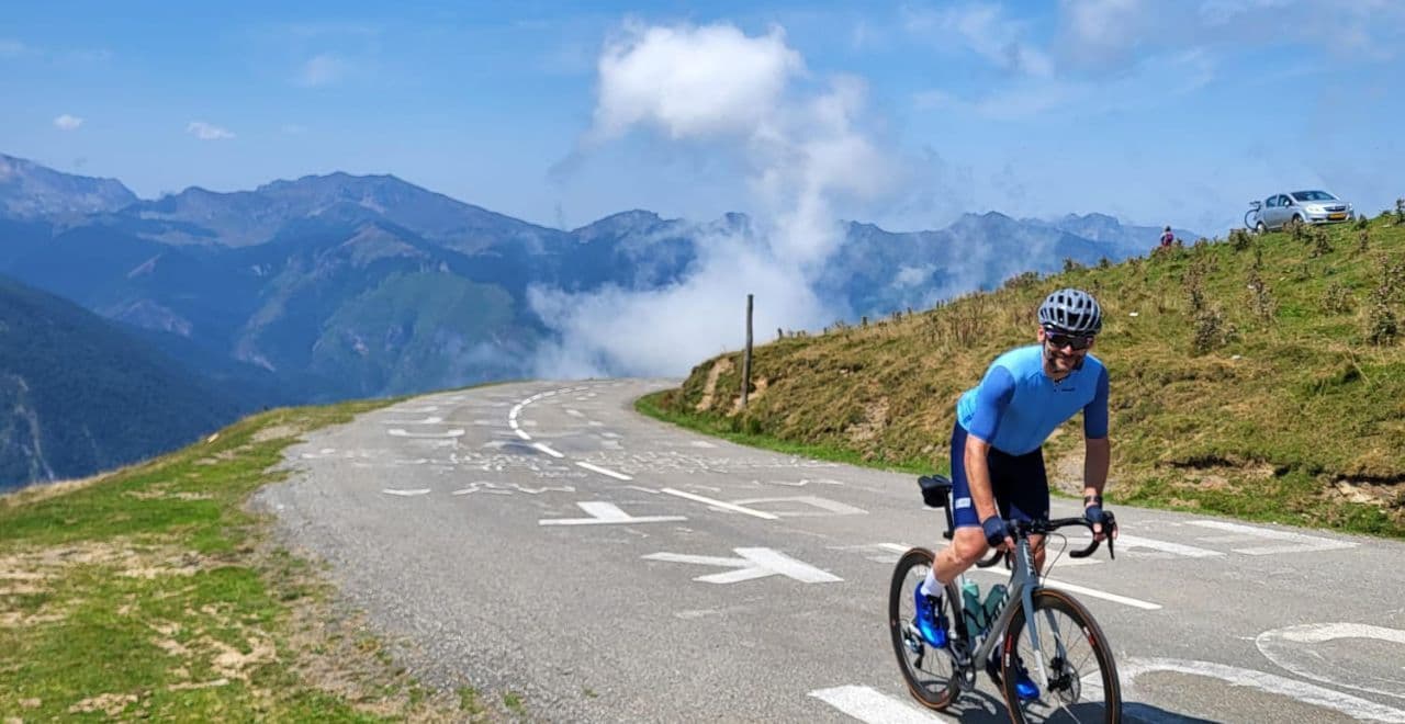 Cyclist riding uphill on mountain road with panoramic cloudy sky and distant peaks