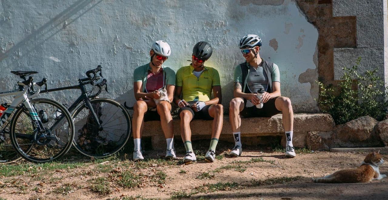Three cyclists relaxing on bench with cat and road bikes nearby