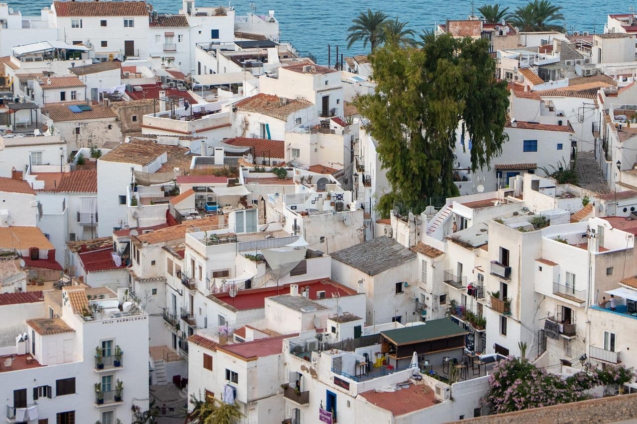Aerial view of Ibiza’s old town with white Mediterranean houses, red-tiled roofs, and lush greenery near the sea.