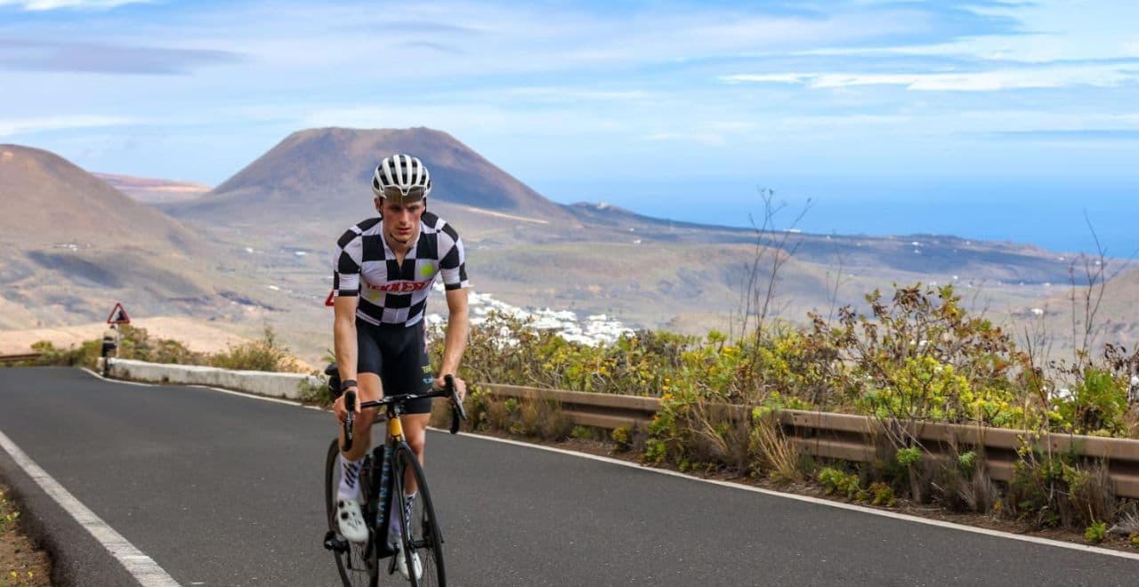 Cyclist in checkered jersey riding uphill with volcano and sea view