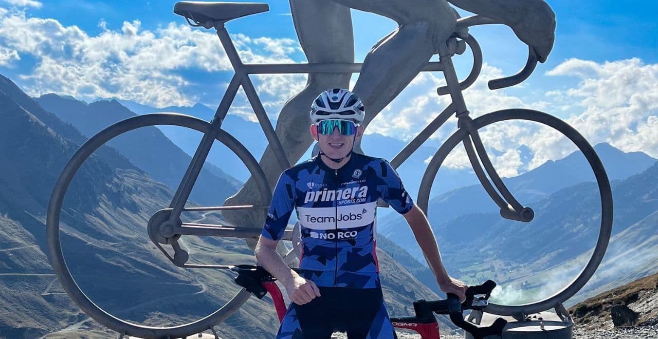 Cyclist posing with bike in front of giant mountain cycling monument under blue sky