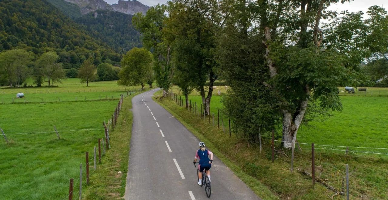 female cyclist riding a flat road between fields with mountains in the distance