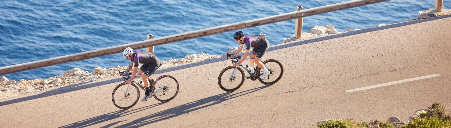 2 cyclists riding down a coastal road in single file