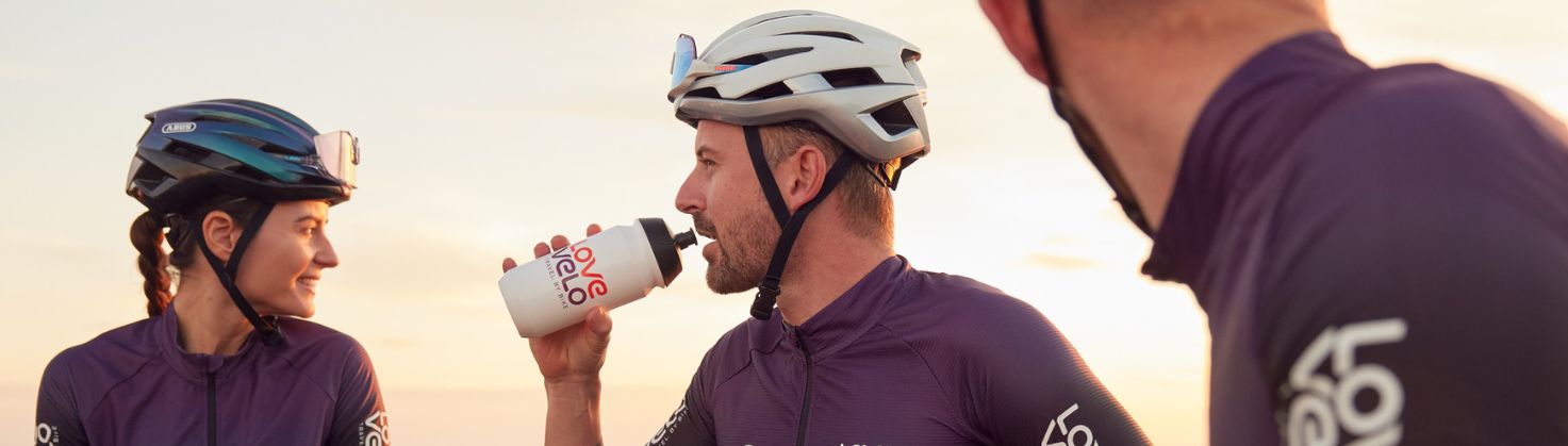 male cyclists drinking from a water bottle with female cyclists looking at the sunrise behind her