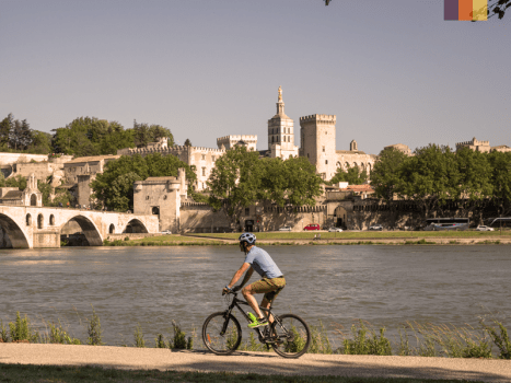 a cyclist travels along a traffic free path beside a river in a historic provence town, france