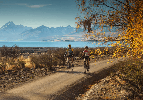 two cyclists on the alps to ocean cycle trail with mountains in the background