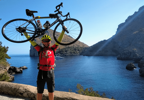 a cyclist holds up their bike beside the sea in mallorca