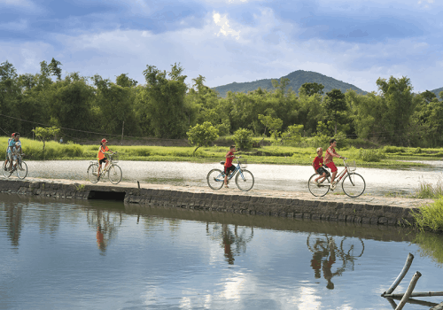 vietnamese children cycle across a stone bridge over a river
