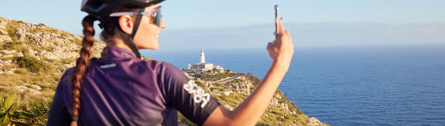 Girl on bike taking selfie on mountain looking over lighthouse