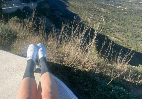 girl's legs sitting on a wall looking over a road in Spain