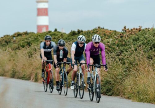 4 cyclists riding in a line with a lighthouse in the distance