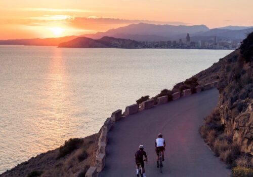 2 cyclists riding at sunset along a coastal road in Calpe, Spain