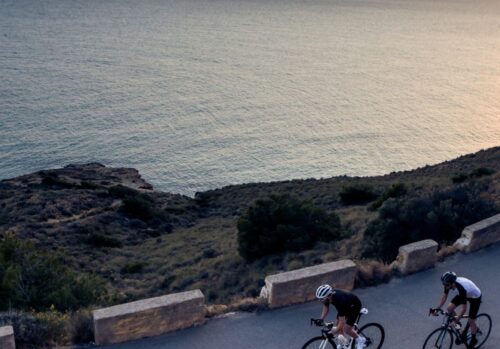 2 cyclists riding on a coastal road with the sea next to them in Calpe, Spain