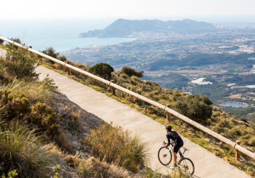 Single cyclist riding on a hill with the city of Calpe and the coastline below