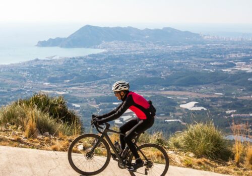 Single cyclist riding up a hill with the city and the coastline below